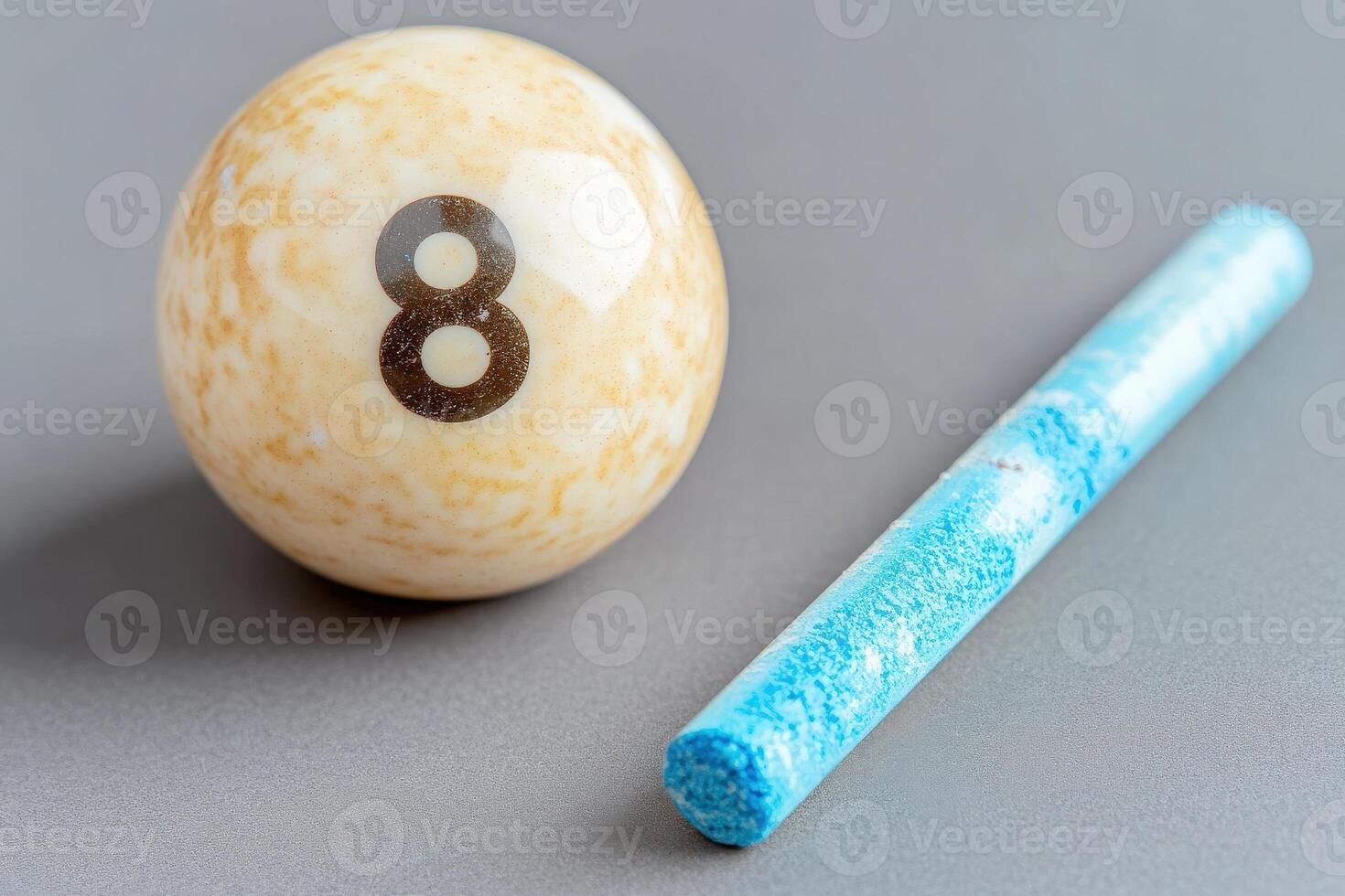 A solitary snooker ball rests next to a piece of blue cue chalk on a smooth gray surface, emphasizing the essentials of cue sports in a minimalist setting ideal for focusing on the game. photo