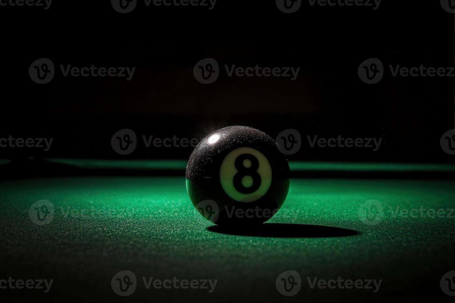A single black snooker ball lies perilously on the edge of a green felt surface, illuminated by soft lighting that highlights its glossy finish and the surrounding shadows. photo