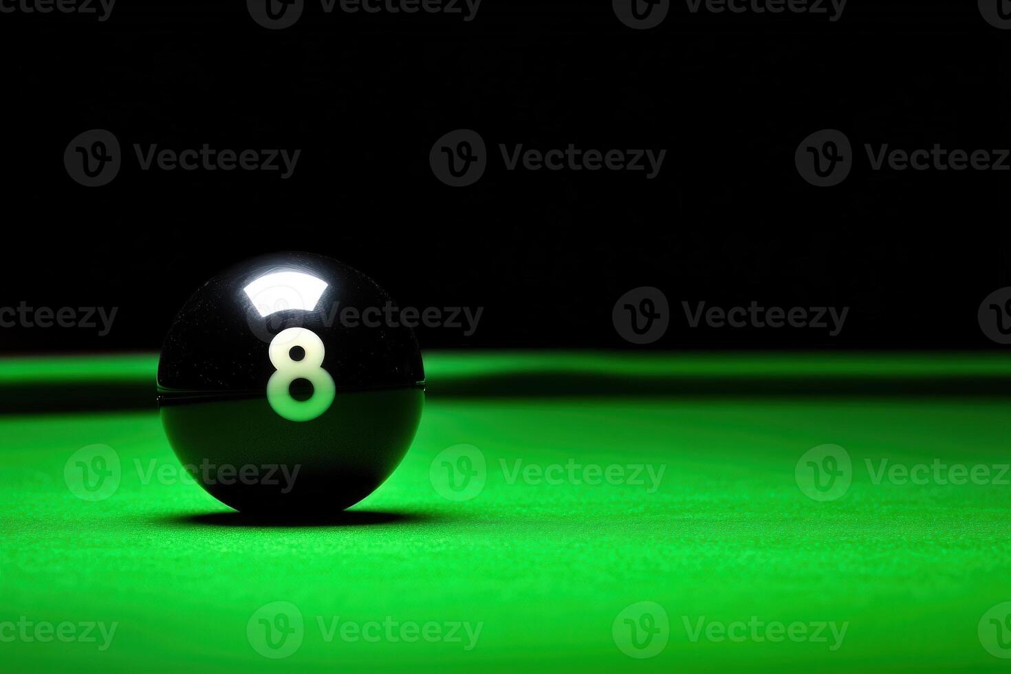 A single black snooker ball rests precariously on the edge of a green table, surrounded by a shadowy atmosphere. The low lighting highlights the glossy surface and the number eight. photo