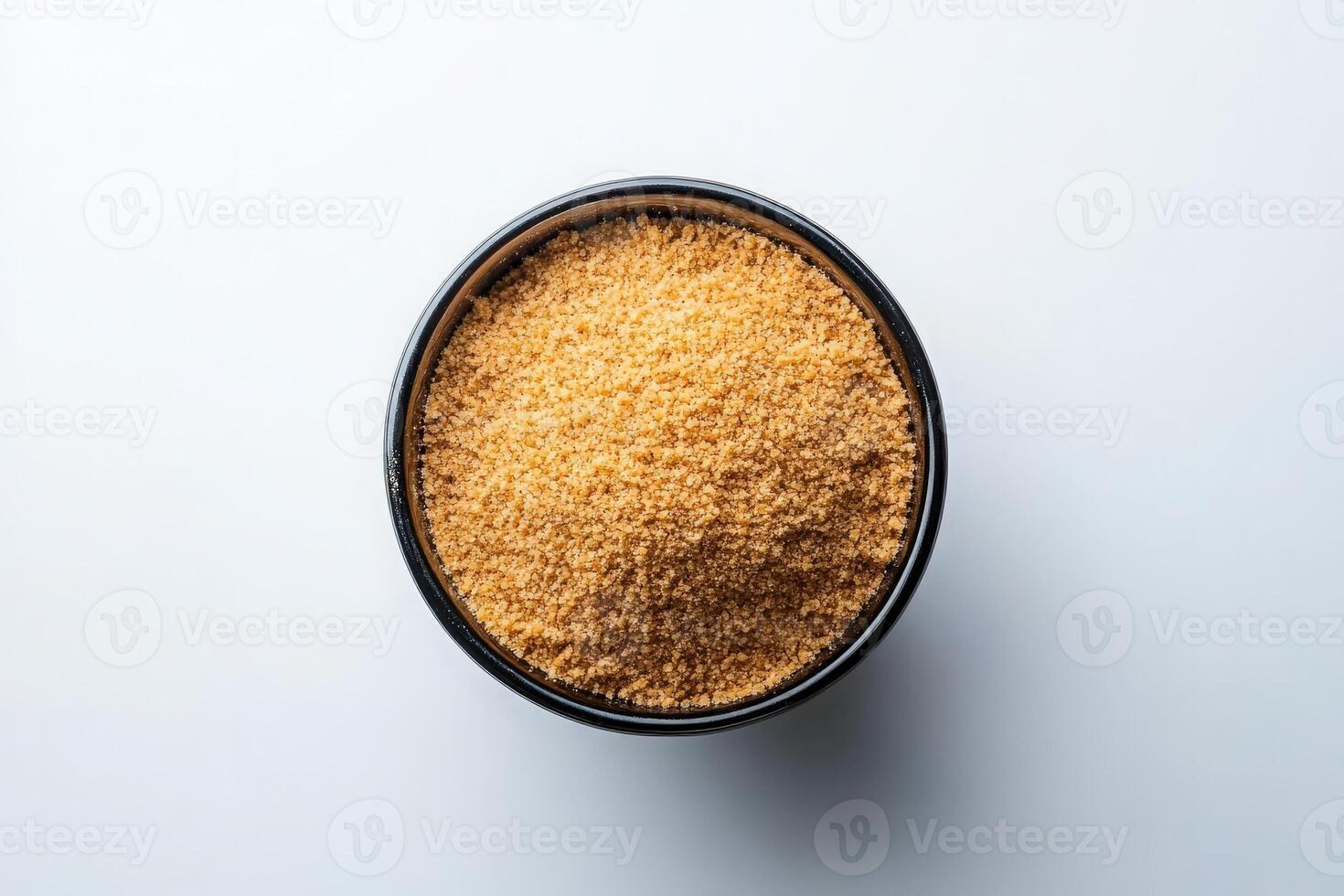 A black bowl filled with finely crushed graham cracker crumbs is prominently displayed on a light surface, showcasing the golden-brown texture and fine consistency of the crumbs. photo