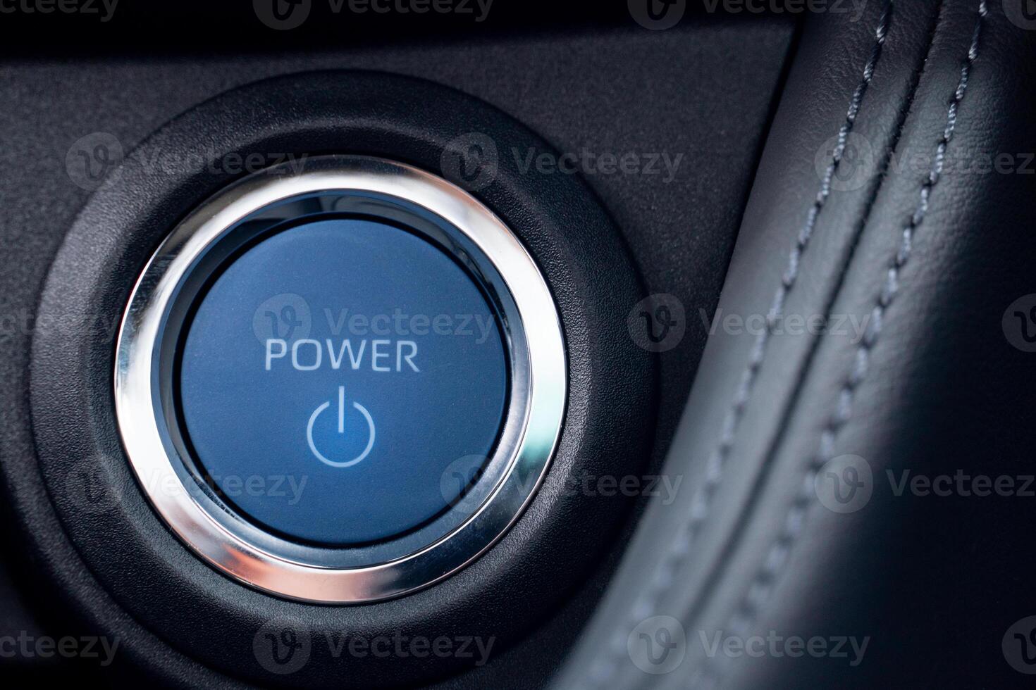 Blue power start engine button with a silver ring surrounding it. The button is illuminated and has a power symbol on it. Button design suggests that it belongs to a modern car model. photo