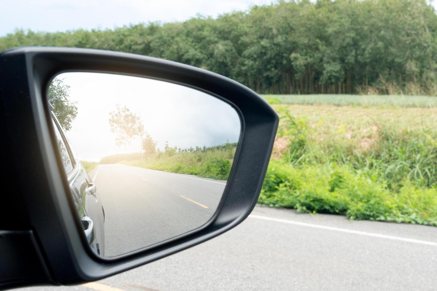 Inside view of mirrors wing. Rear view of a black car with asphalt road and green grass in the daytime. Clear traffic in rural areas. photo