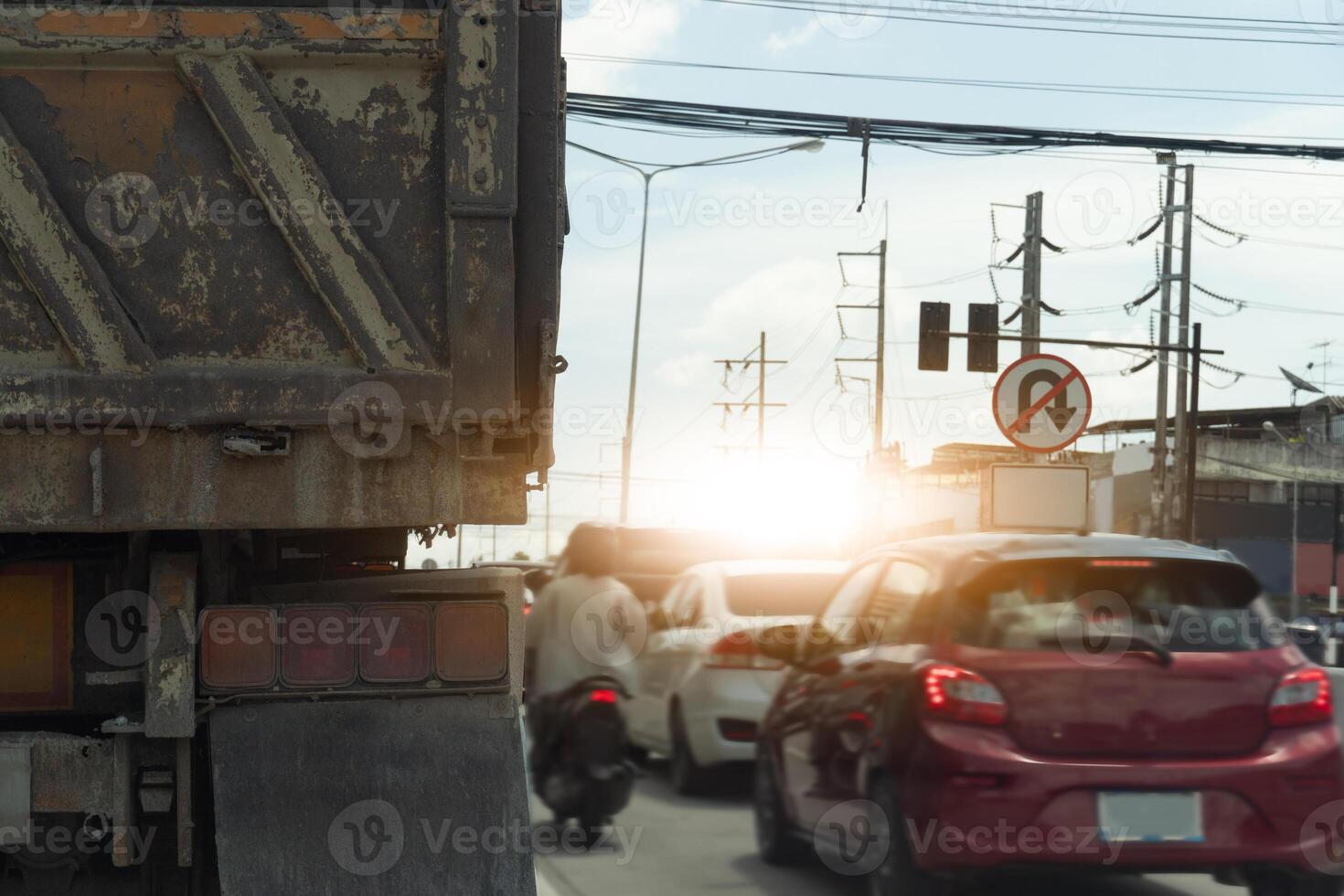 Busy intersection with a variety of vehicles. Including rear side of truck cars and a motorcycle. Sun is setting in the background, casting a warm glow over the scene. photo