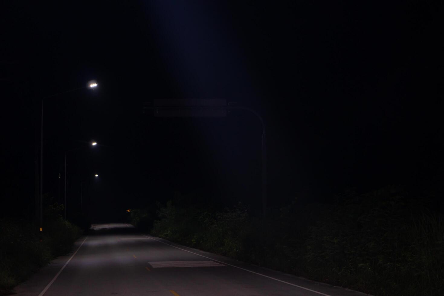Empty road at night. Only light comes from a few street lamps that are illuminating the road ahead. Road is surrounded by trees that are casting long shadows. Scene appears to be quiet and peaceful. photo