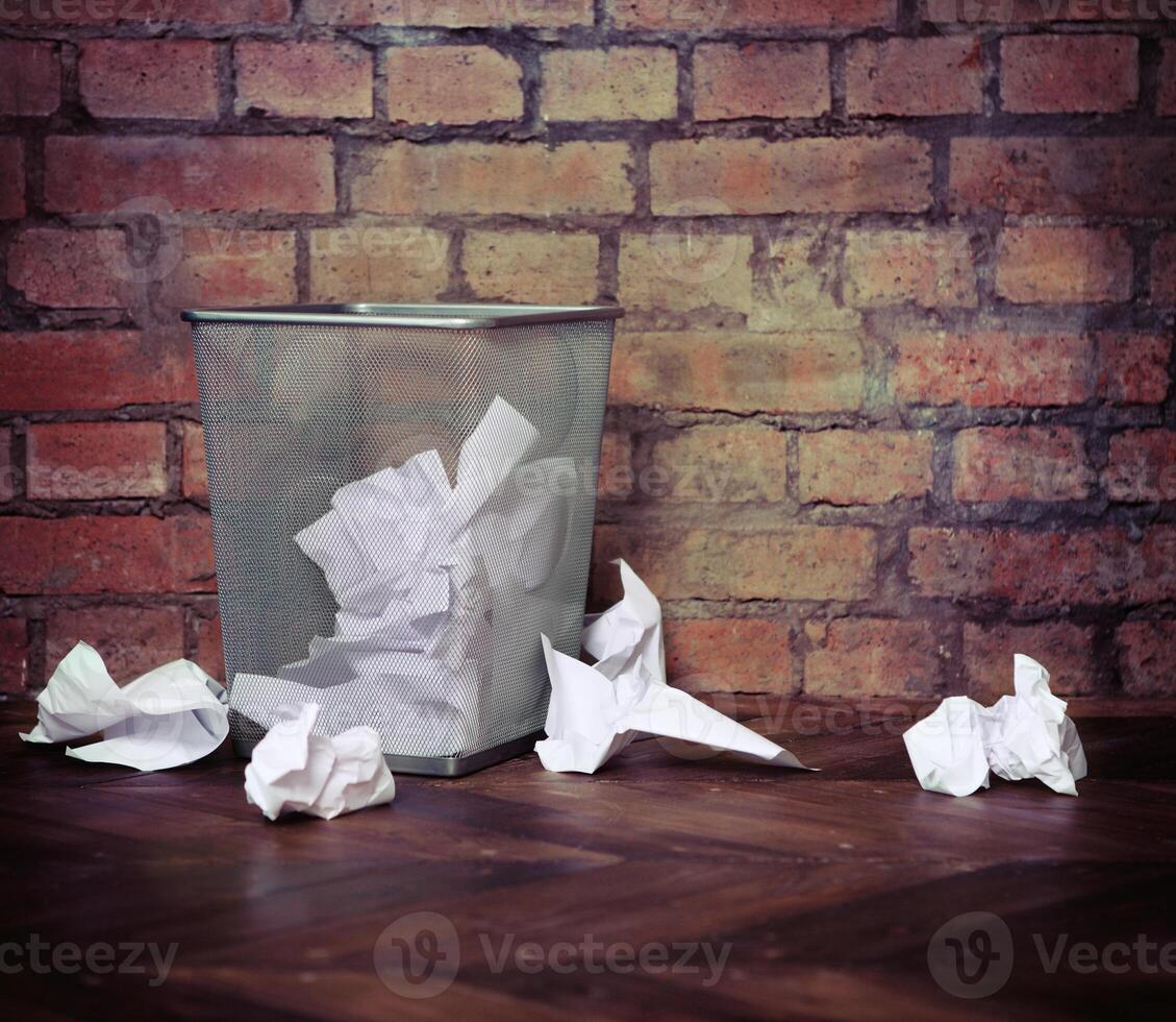 Recycle bin filled with crumpled papers. Brick wall background photo