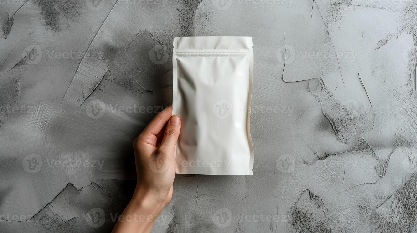 Hand holding white resealable pouch mockup on textured gray background. Minimalist and industrial aesthetic food packaging template advertising image. Cosmetics mock up product photo