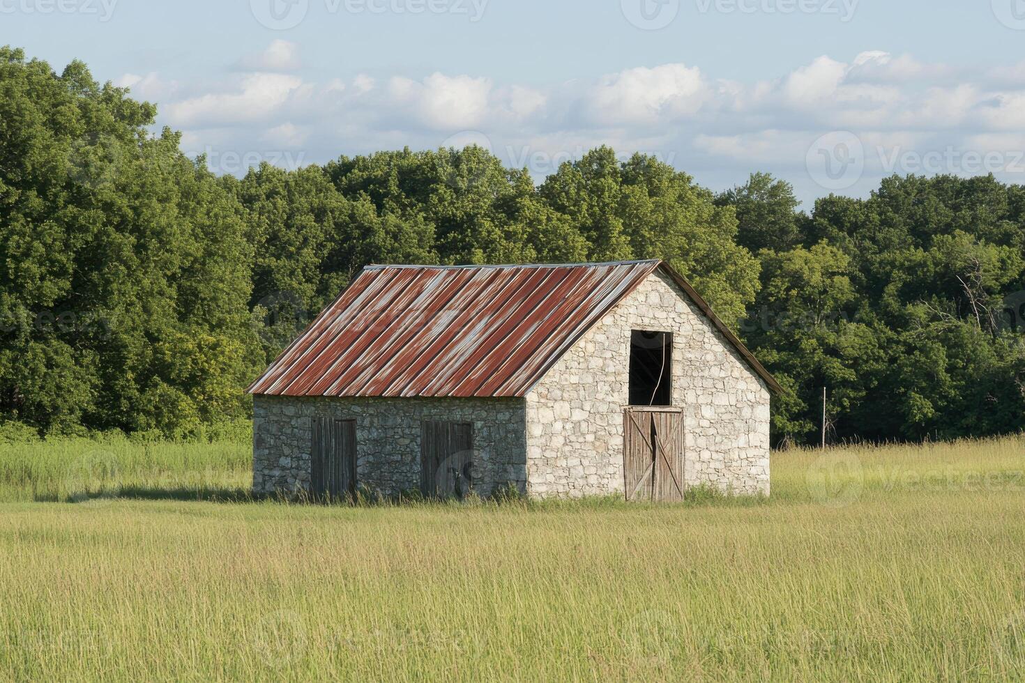 Abandoned stone barn in a field surrounded by trees during a sunny day photo
