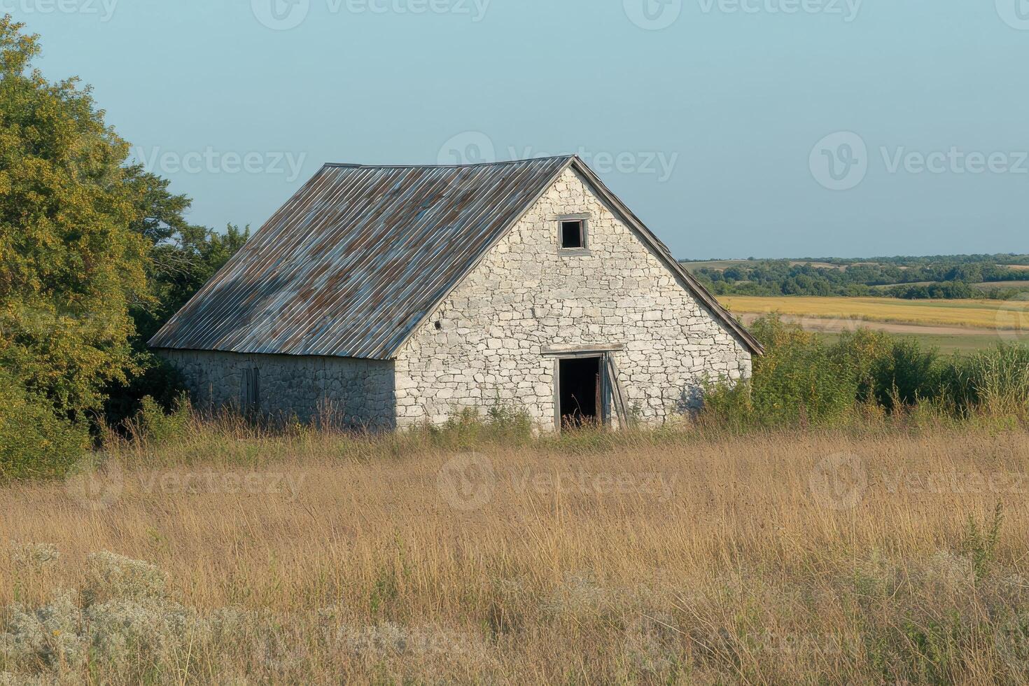 Old stone barn surrounded by tall grass on a clear day in the countryside photo