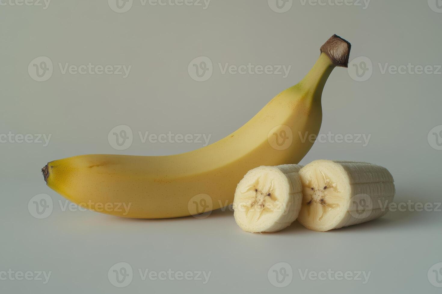 A ripe banana beside two freshly cut banana pieces on a light background photo