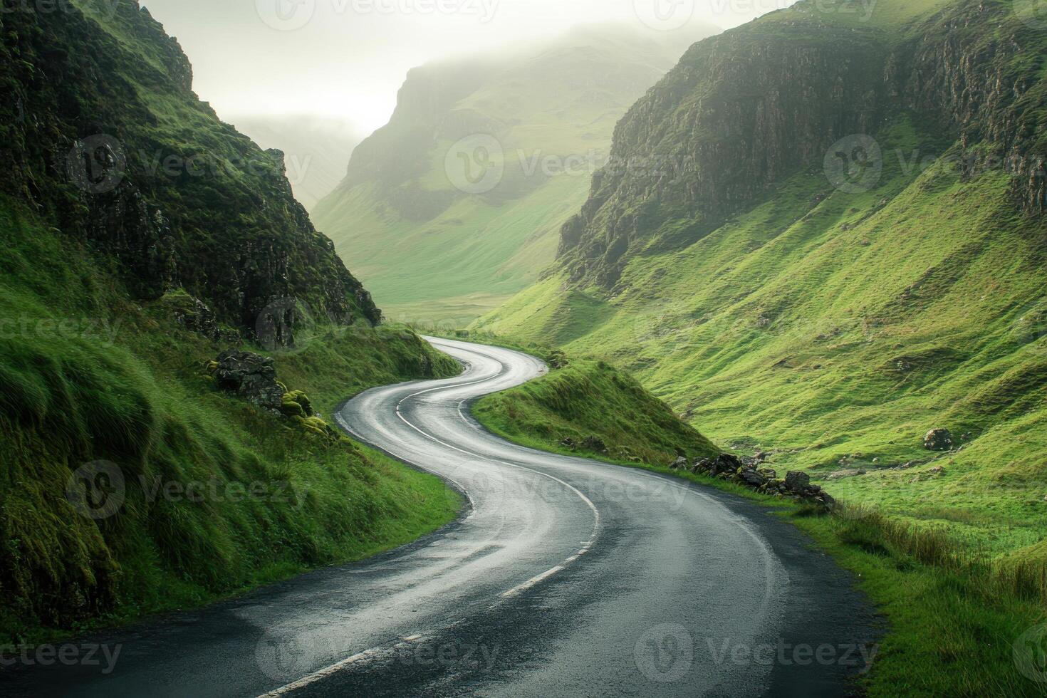 Winding road through lush green hills of a misty valley during early morning light photo