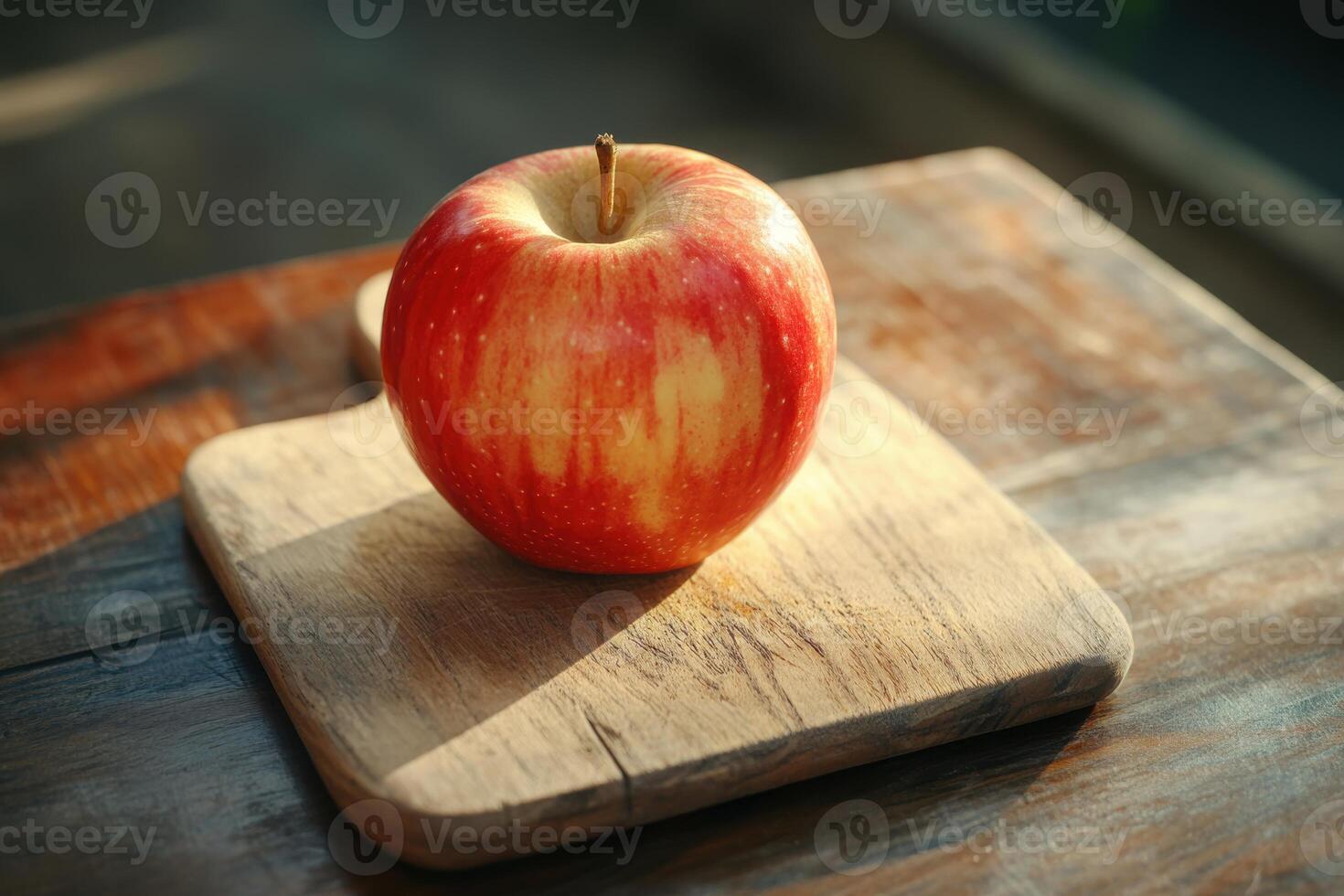 Fresh red apple resting on a wooden cutting board with natural light illuminating it photo