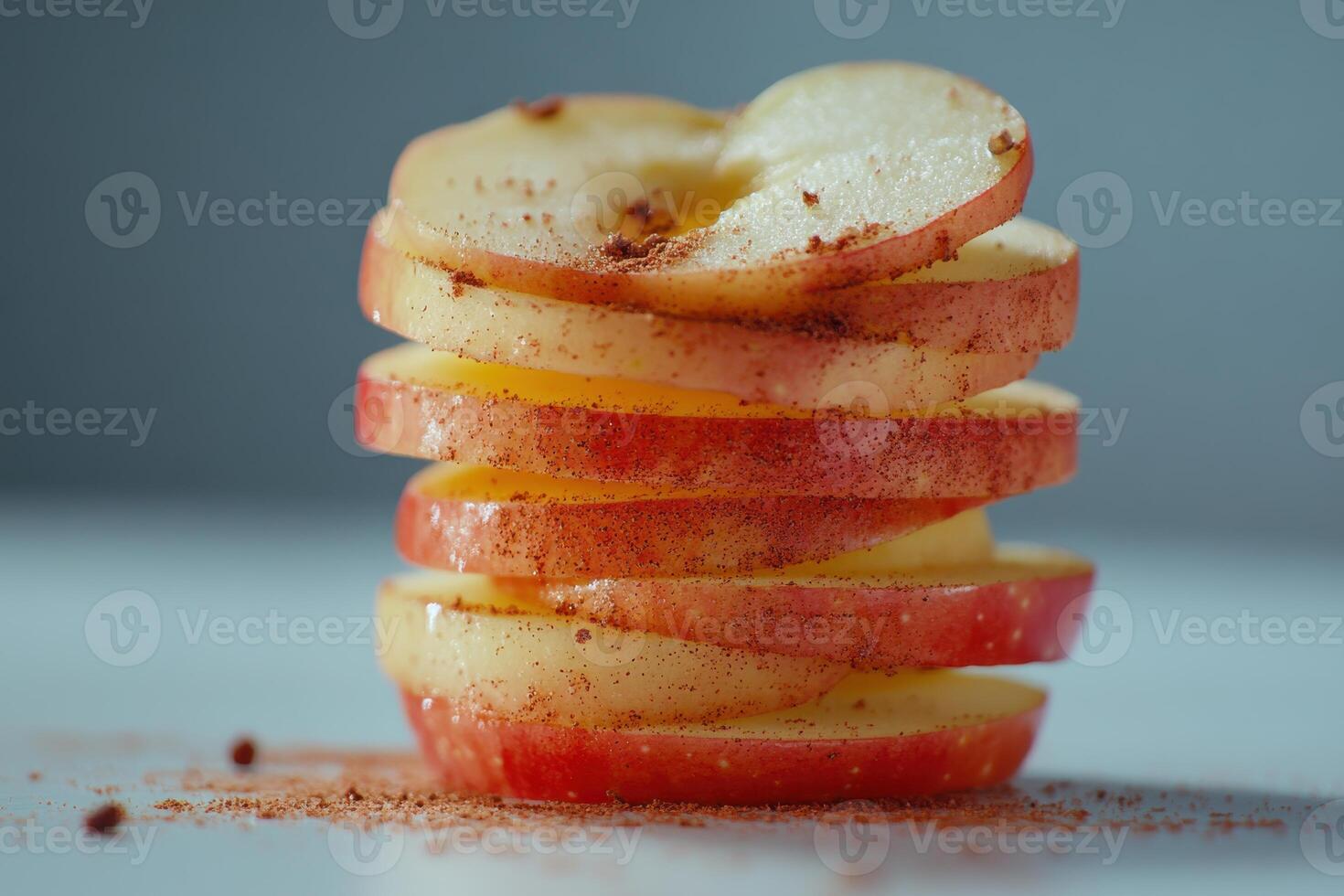 Stacked red apple slices sprinkled with cinnamon on a white surface in natural light photo