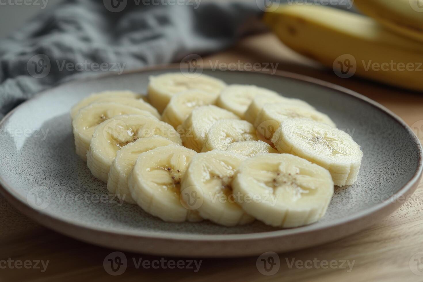 Sliced banana arranged neatly on a plate with whole bananas in the background on a kitchen table photo