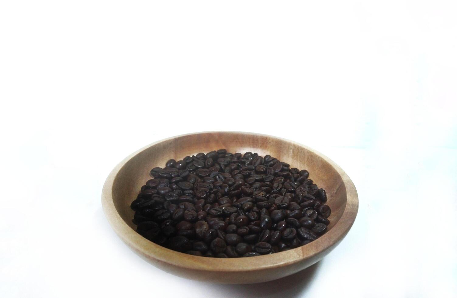 dish of roasted coffee beans on brown wood plate isolated on white background with copy space photo