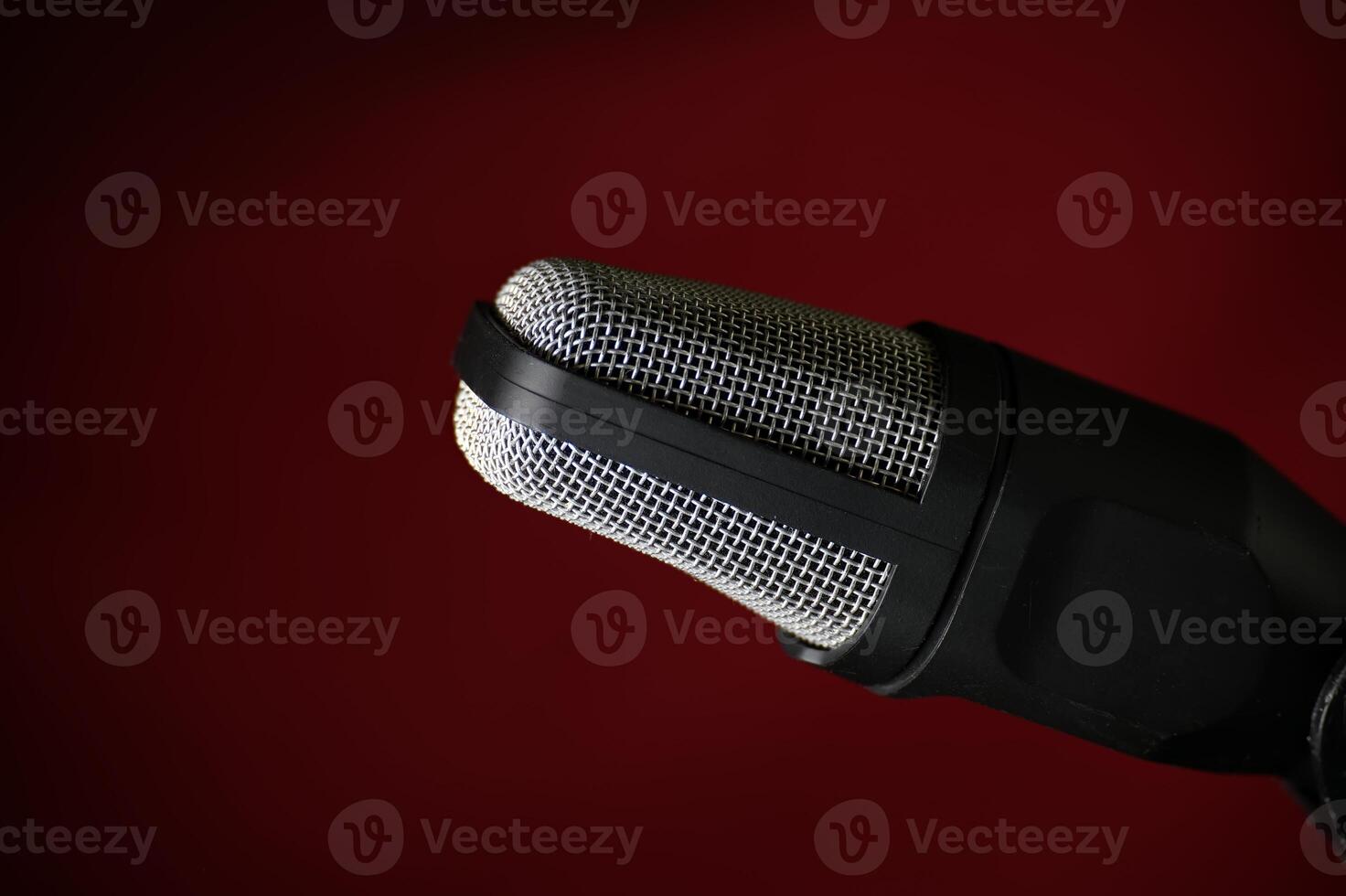 Professional studio microphone with metal mesh grille against dark red background photo