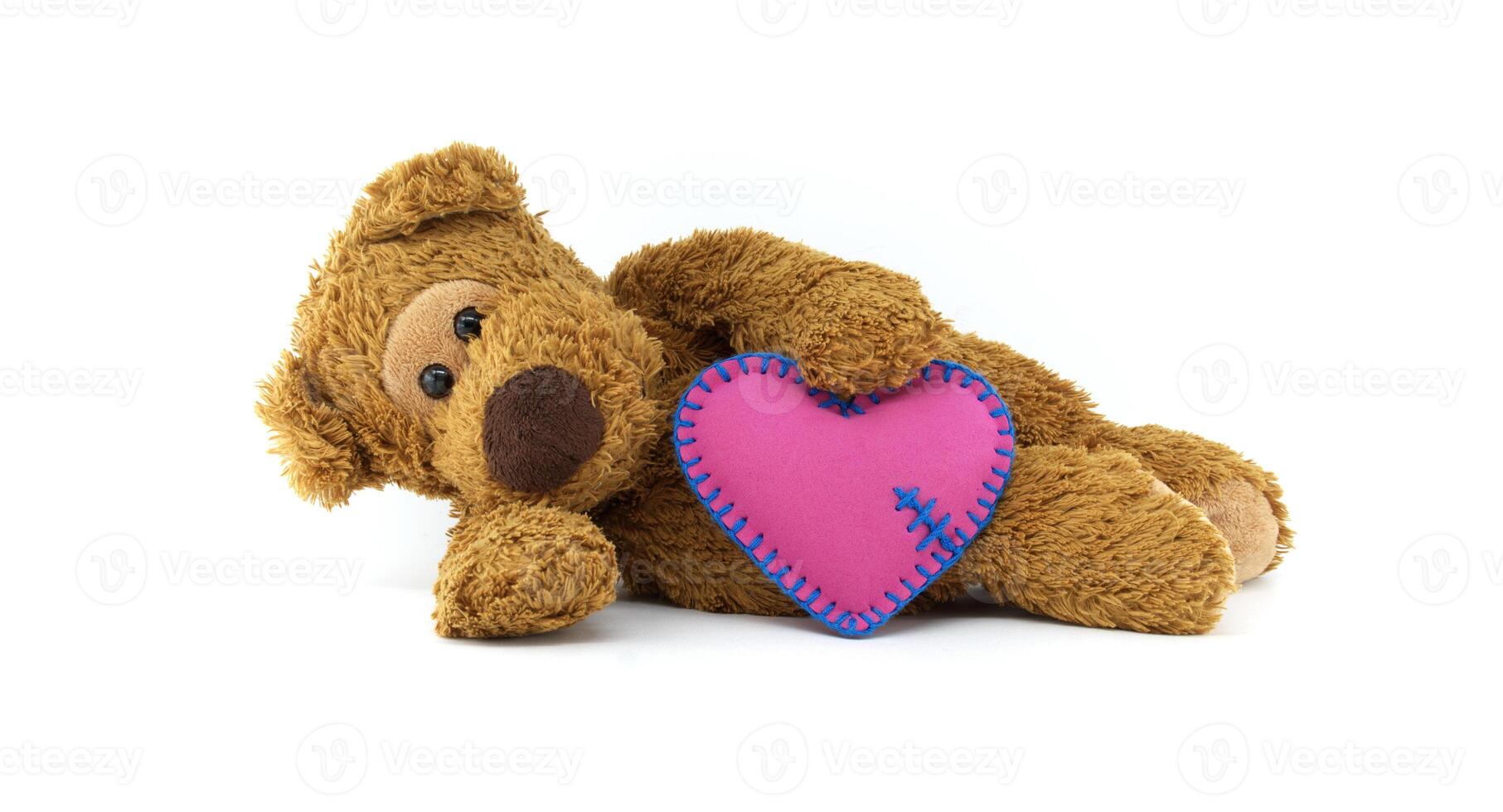 Cute teddy bear holding a pink heart with delicate blue stitching isolated on white background photo