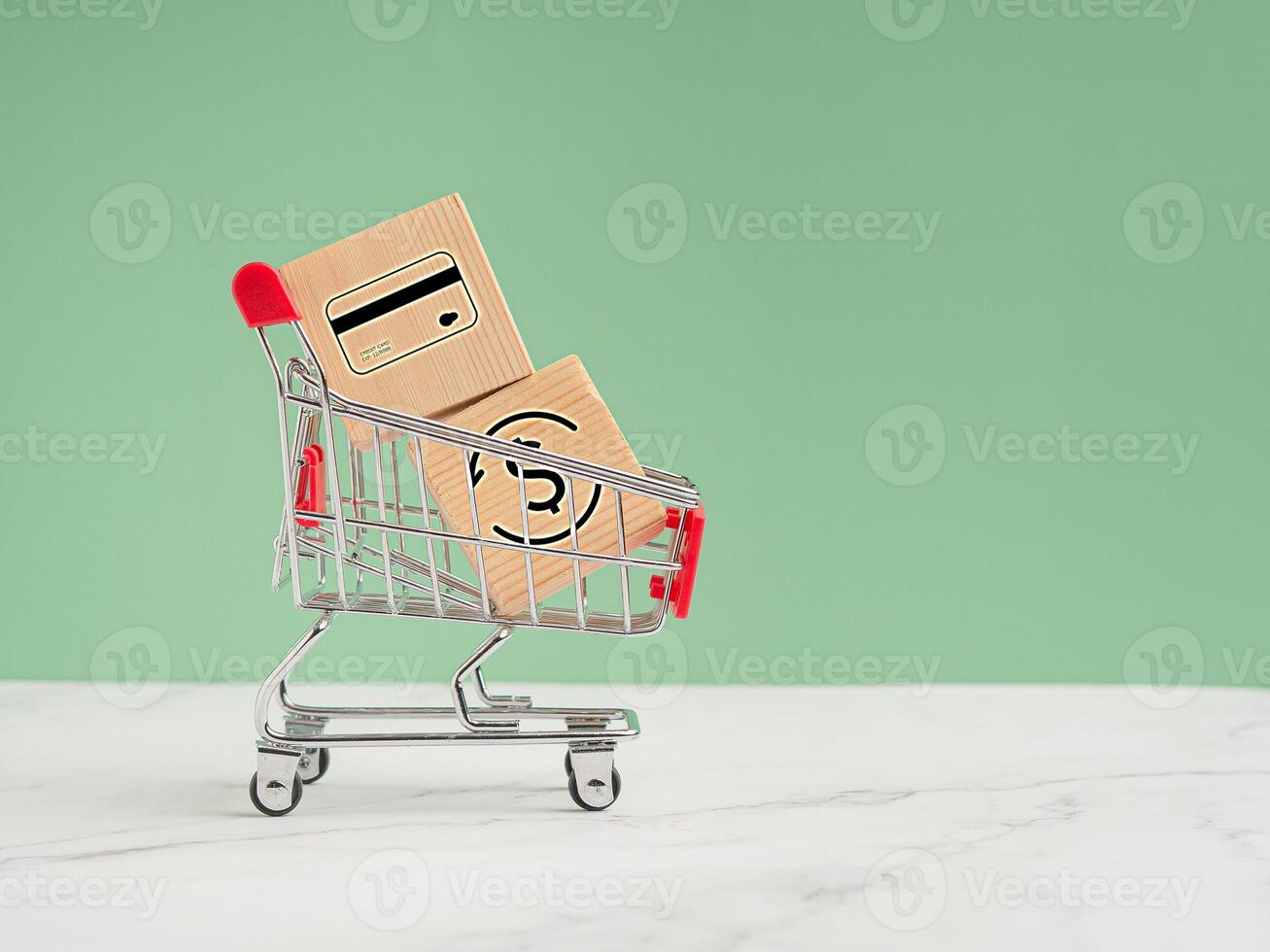 Wooden cubes with finance icons in a mini shopping trolley on the marble floor against a light green background photo