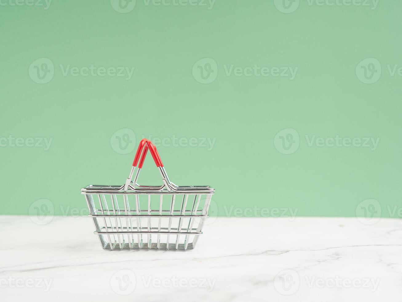 An empty mini shopping cart against a light green background photo