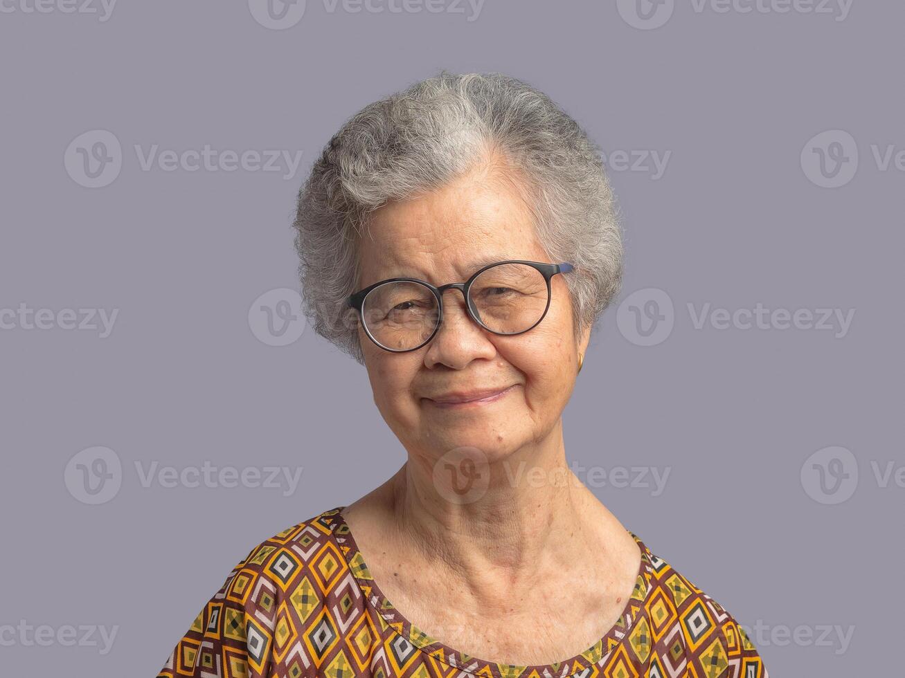 Portrait of a senior woman with short gray hair looking at the camera with a smile while standing on gray background photo