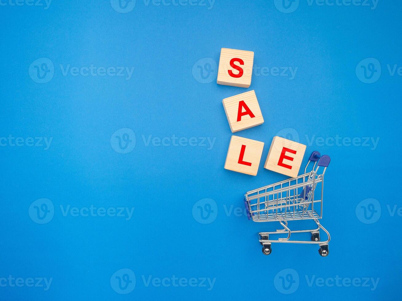 A miniature shopping trolley and wooden blocks with the word SALE over a blue background photo