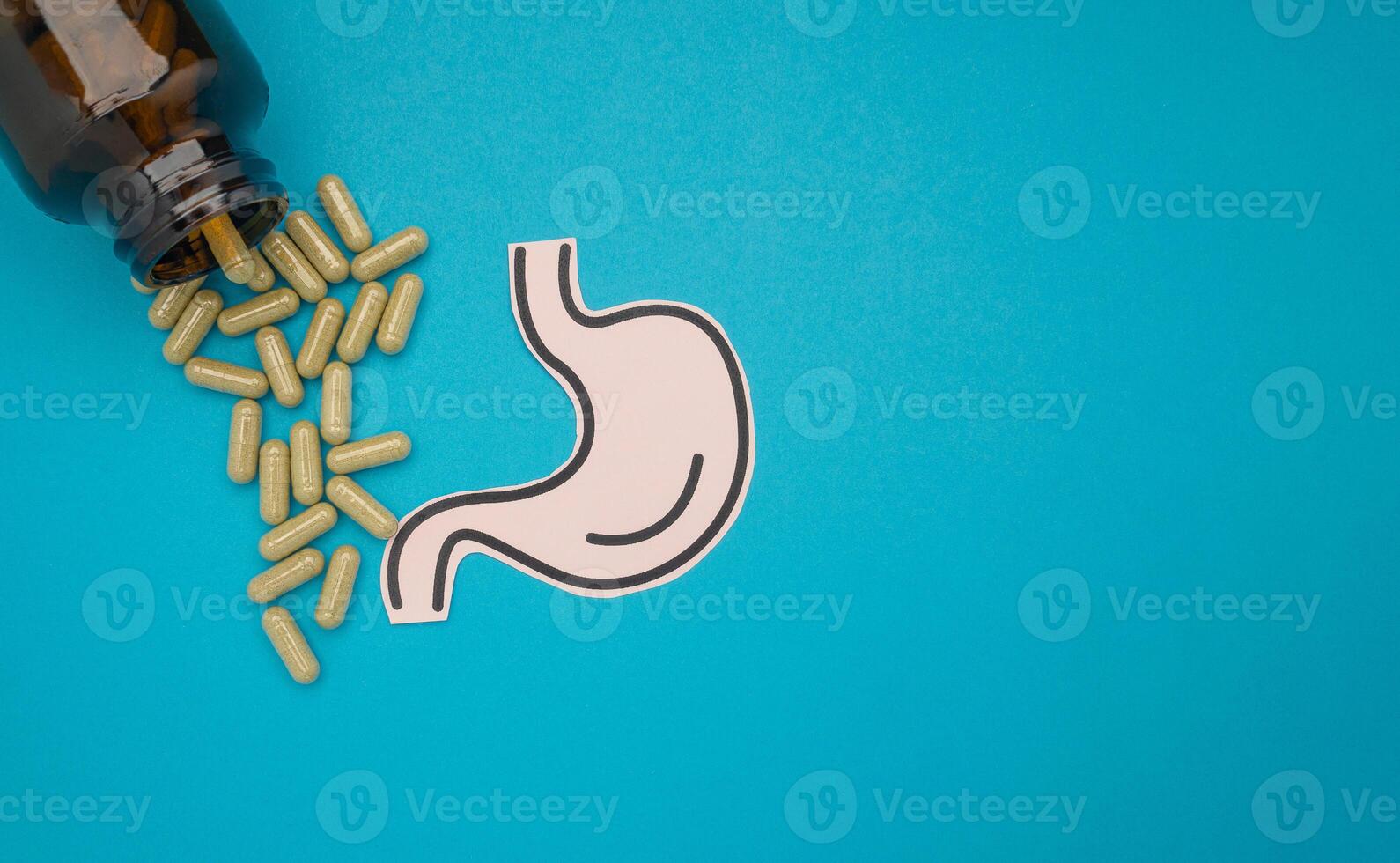 Stomach shape made from paper and pills capsules with a bottle on a blue background photo