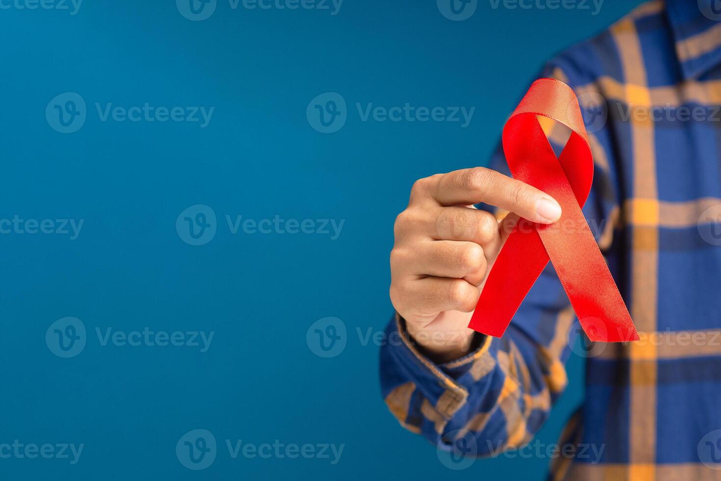 Close-up of hand holding a red ribbon while standing on a blue background photo