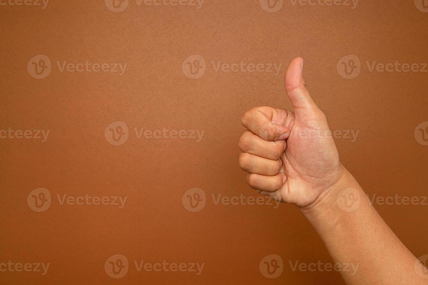 Close-up of hand showing thumbs up gesture against a brown background photo