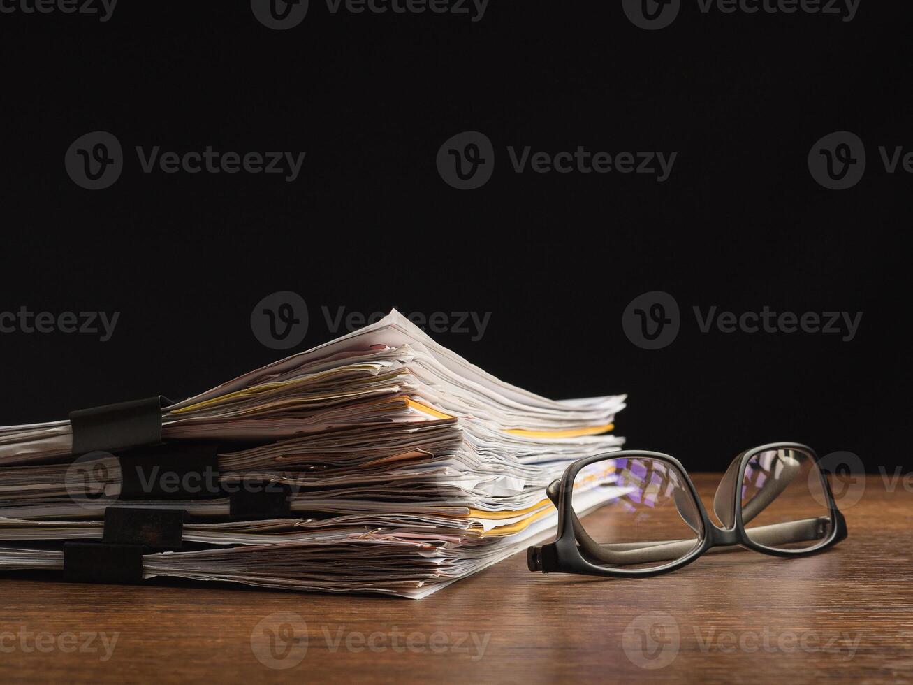 Stack of documents with binder clips and eyeglasses on a wooden table photo