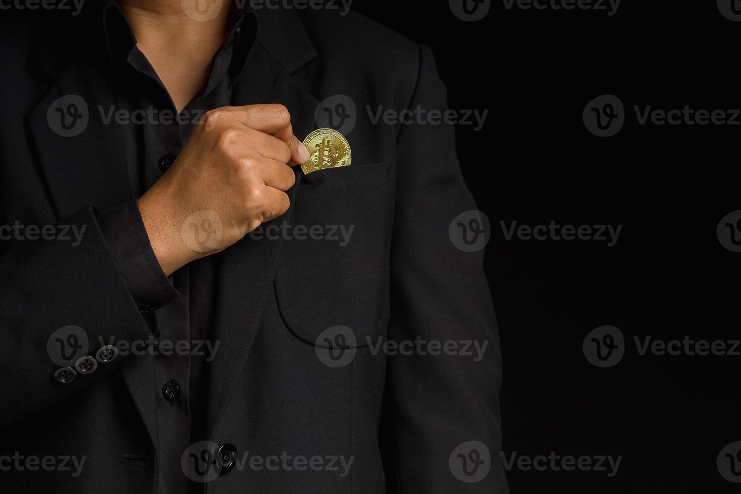 An investor guy holding a bitcoin golden coin put to suit pocket while standing on a black background photo