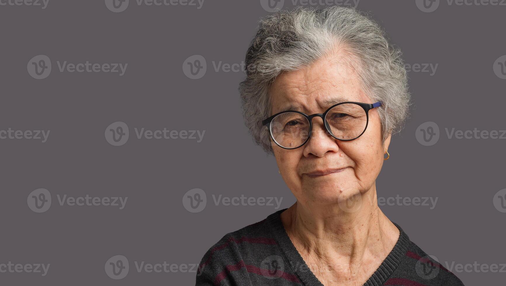 Portrait of a senior woman with short gray hair looking at the camera with a smile while standing on gray background photo