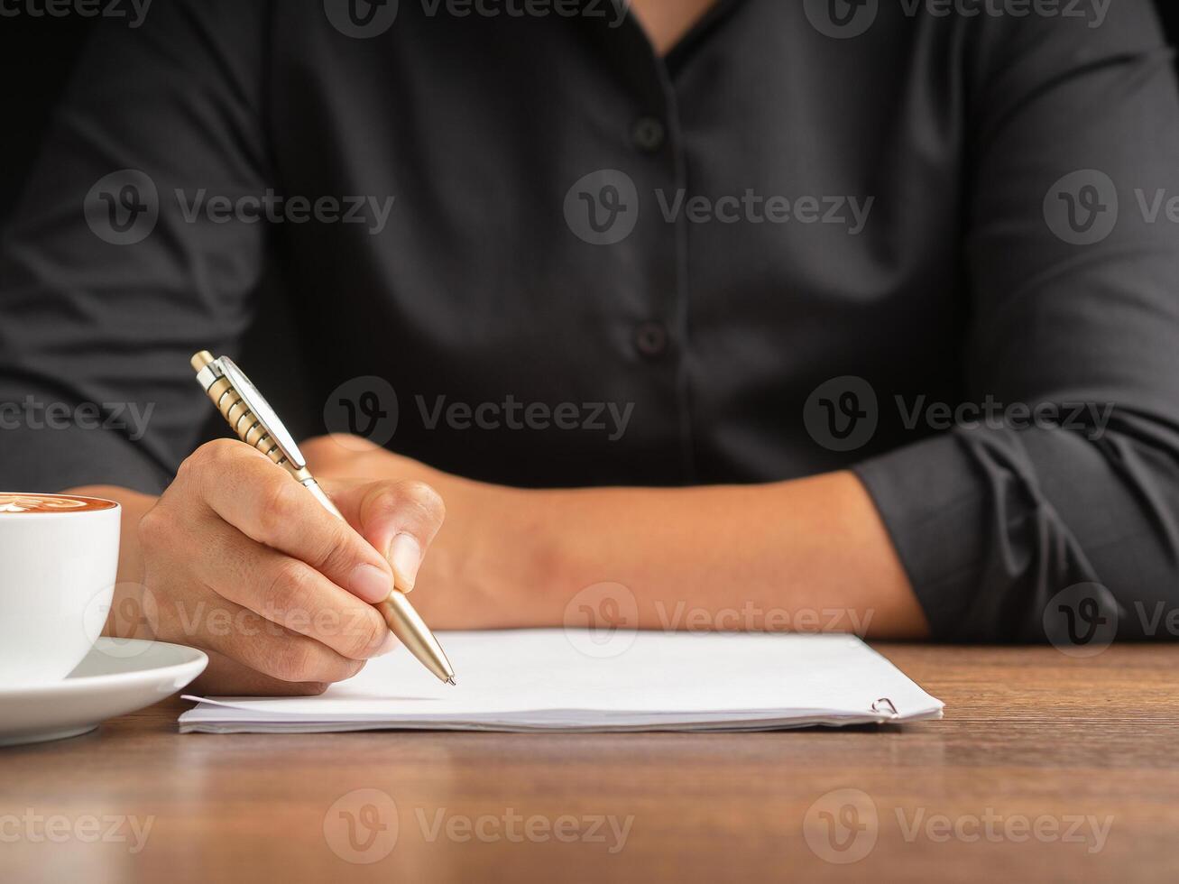 Close-up of a businessman holding a pen writing on paper on a desk while sitting in the office photo