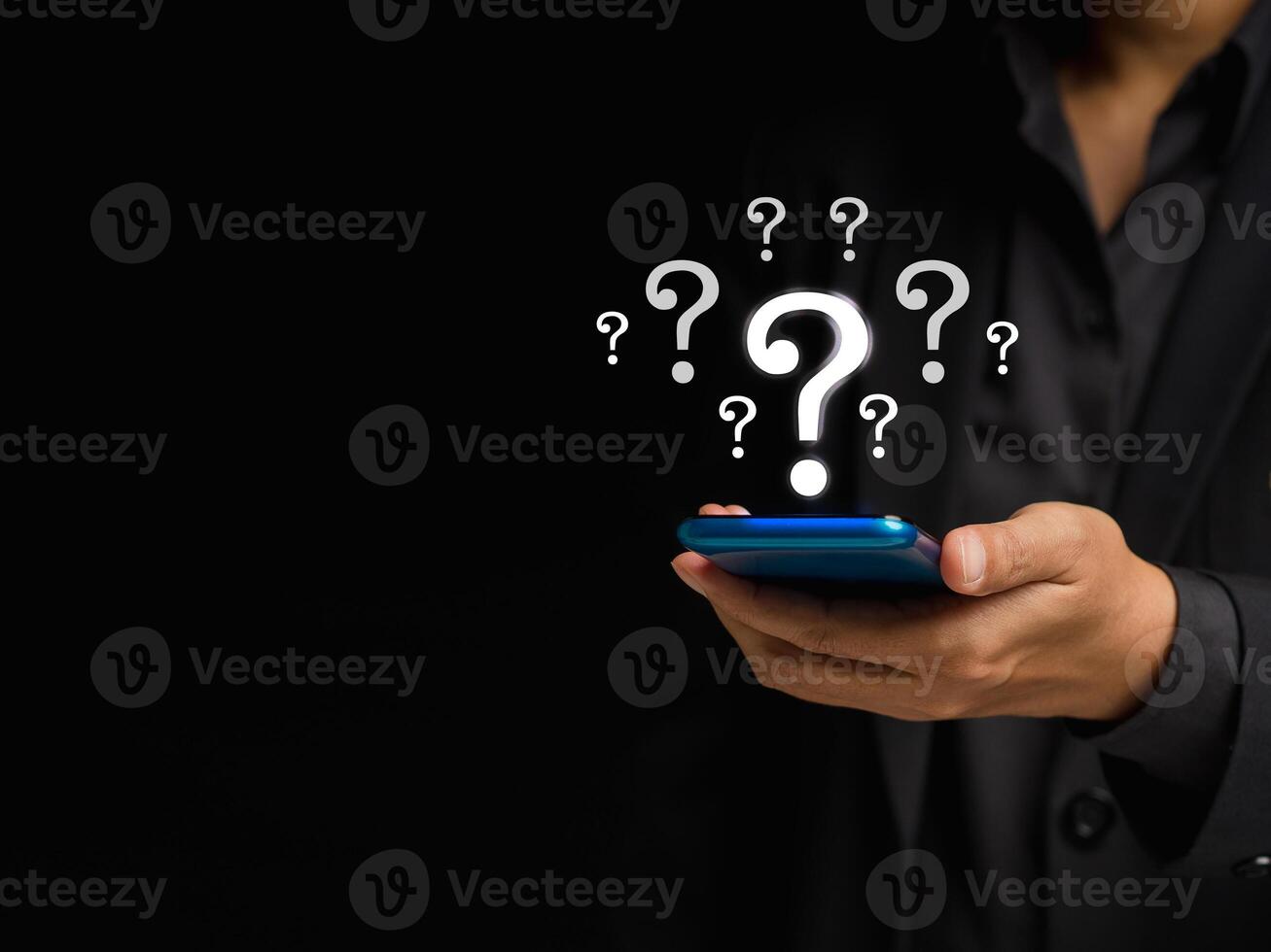Businessman using a smartphone with question marks on a virtual screen while standing on a black background photo