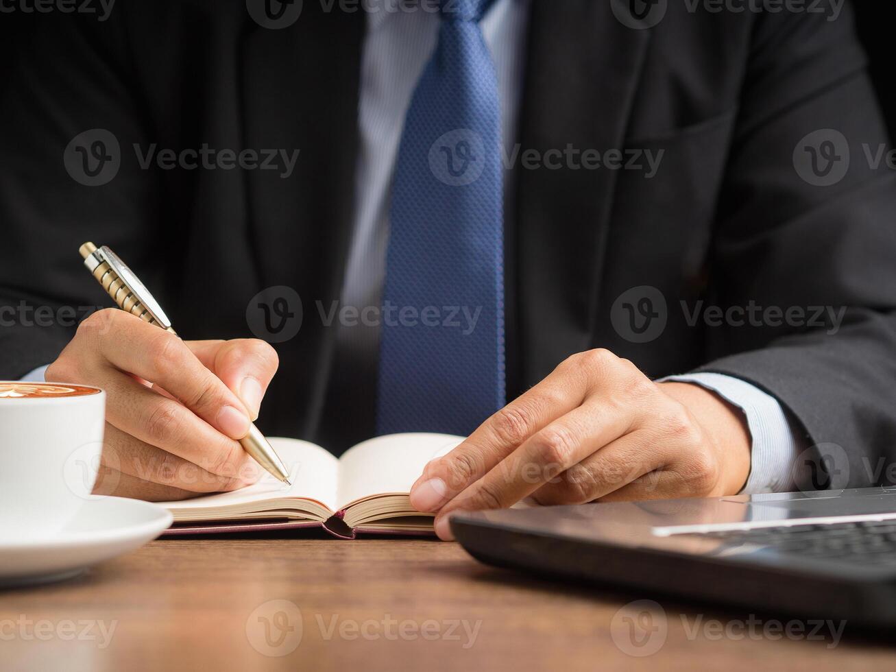 Close-up of a businessman holding a pen writing on paper on a desk while sitting in the office photo