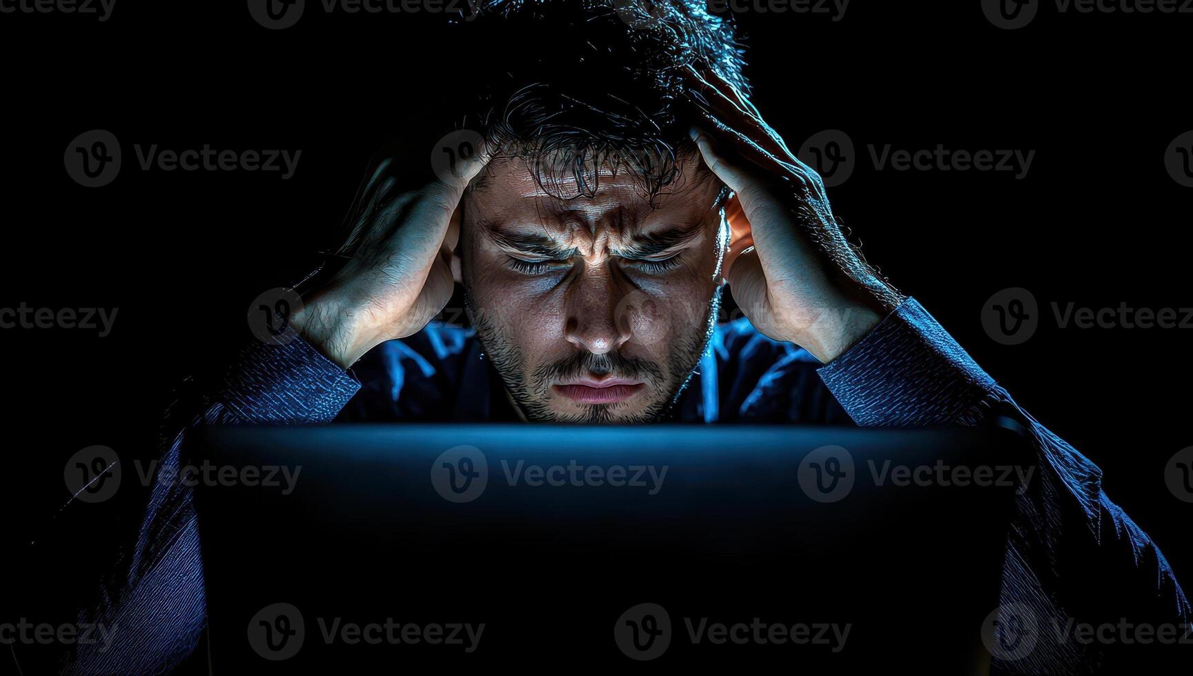 Stressed man working on laptop in dark room. Concept of burnout, stress, and frustration. photo