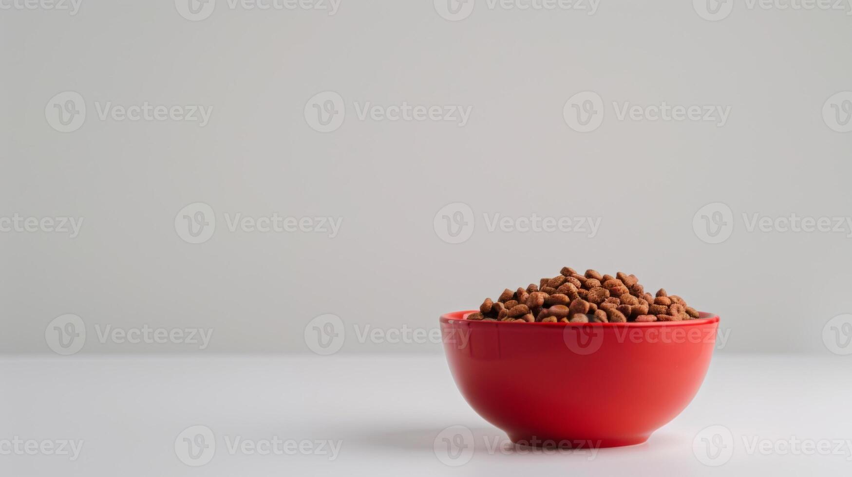 A vibrant red bowl sits on a solid white surface, filled with dry cat food ready for feeding. The scene conveys a sense of care and preparation for pets photo