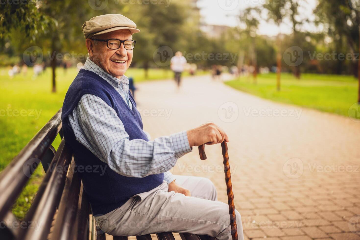 Portrait of happy senior man in park. He is sitting on bench and enjoying autumn day. photo