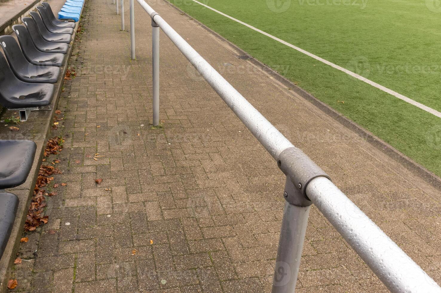 Empty bench and metal railing overlooking artificial turf soccer field photo