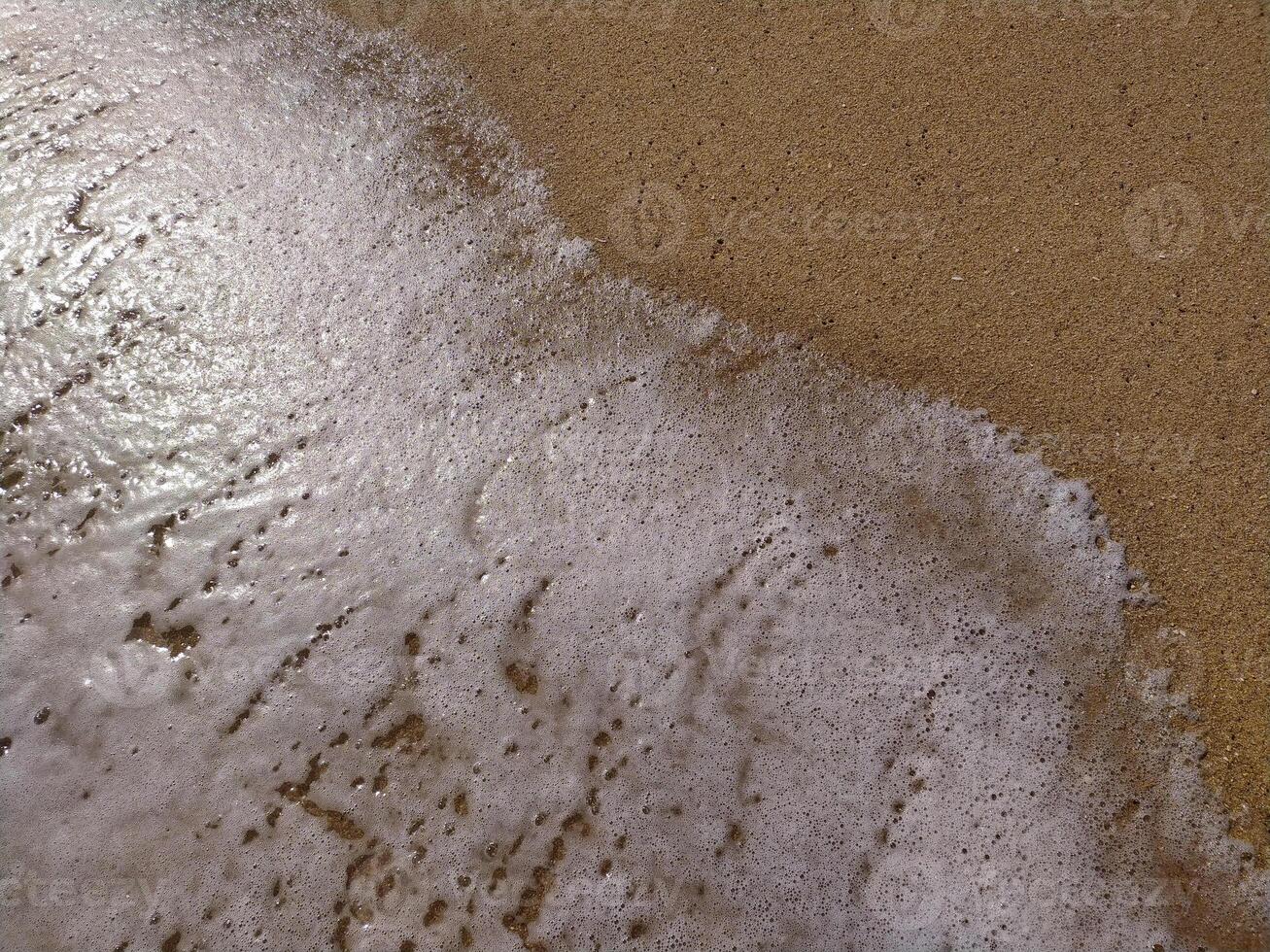 Gentle waves rolling onto sandy beach at sunrise, creating bubbles and a shimmering surface photo