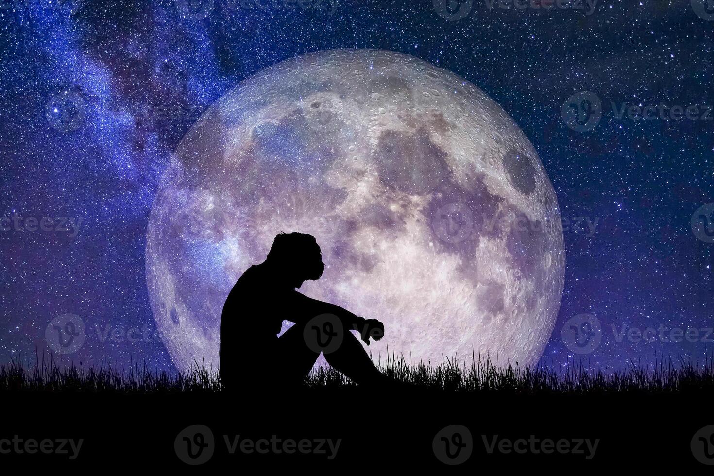 Silhouette of a Person Sitting in Front of a Large Full Moon with a Starry Night Sky Background photo