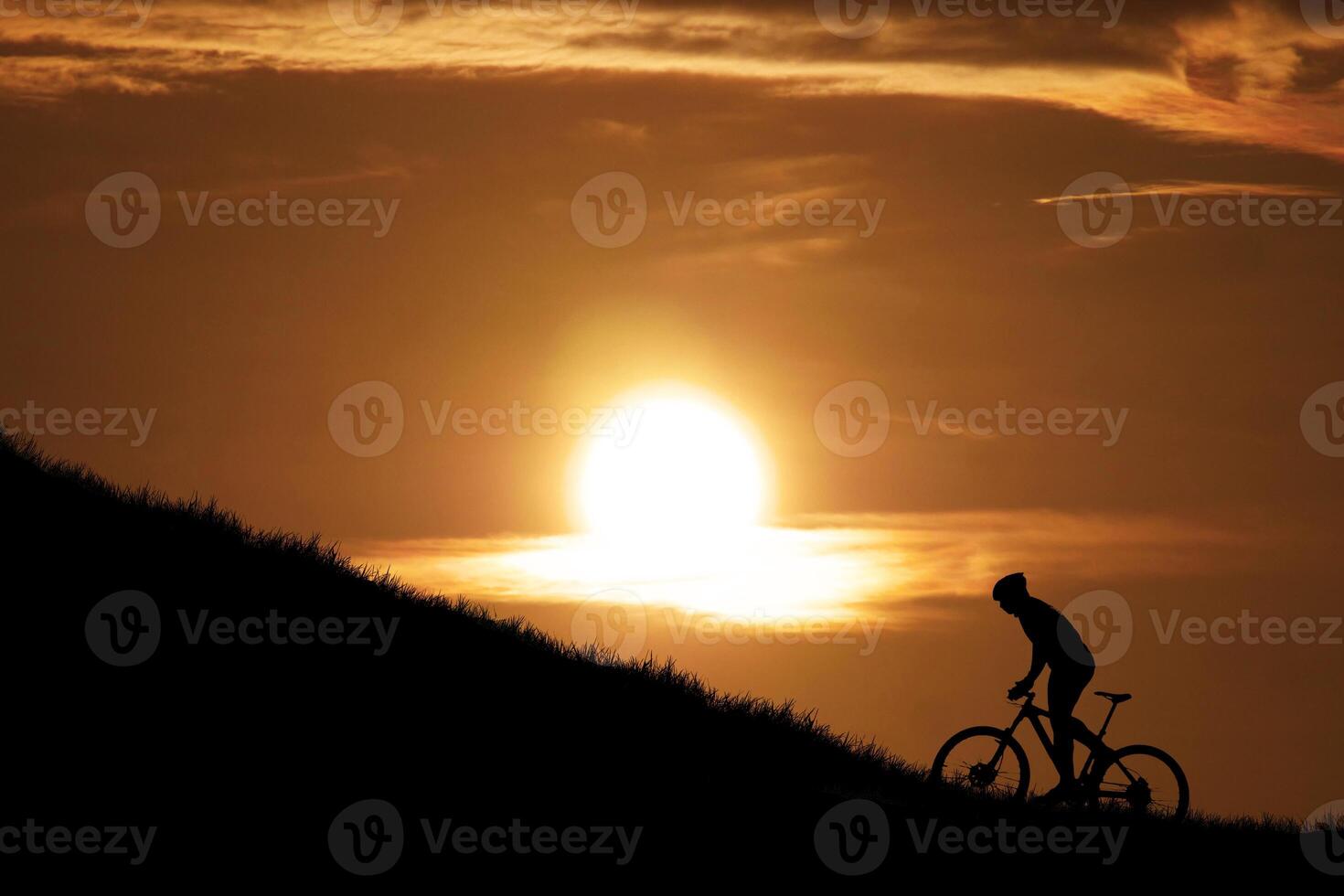 Silhouette of Cyclist Riding Uphill Against a Stunning Sunset Sky with Golden Sunlight and Dramatic Clouds photo