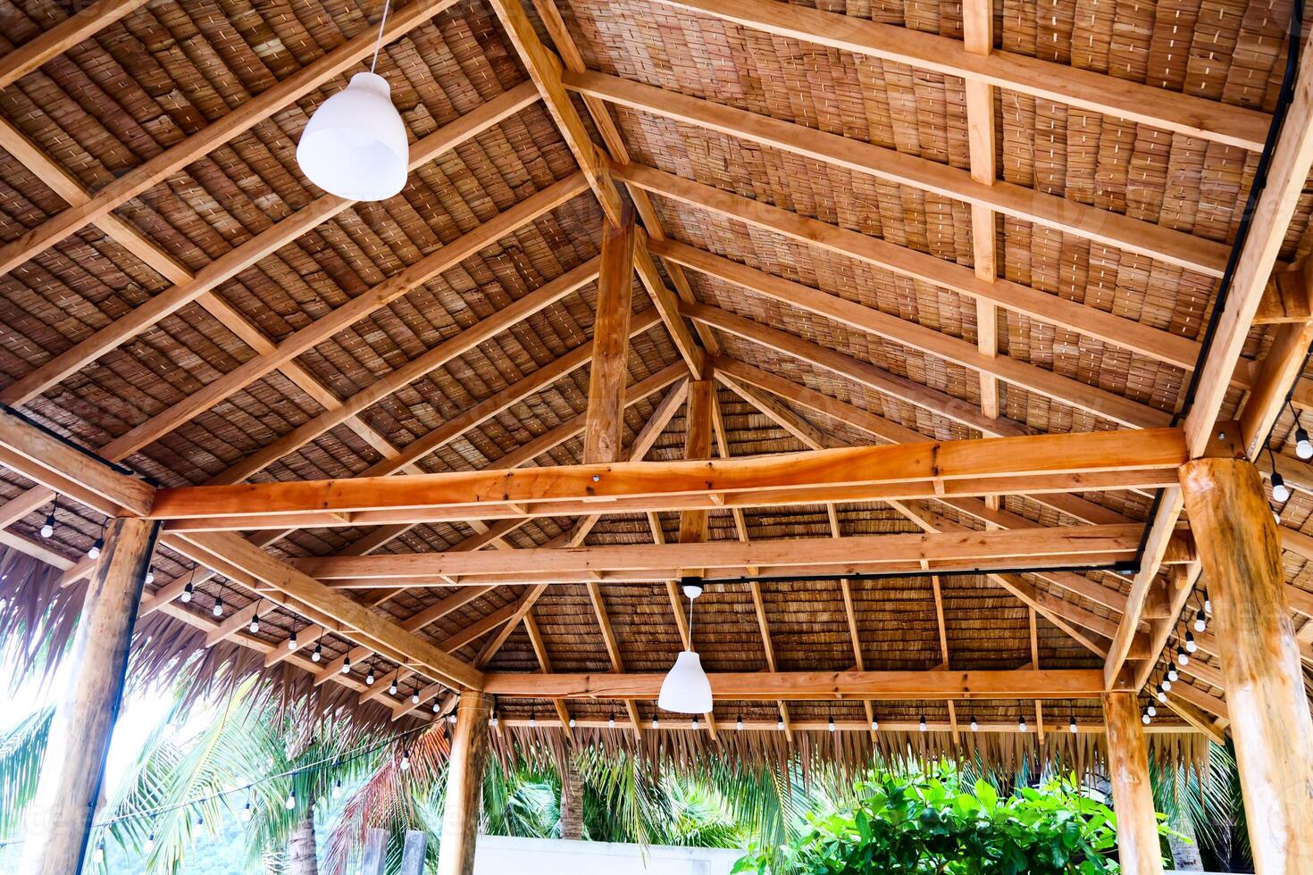Rustic Wooden Gazebo Ceiling with Exposed Beams and Hanging Lights in a Tropical Setting photo