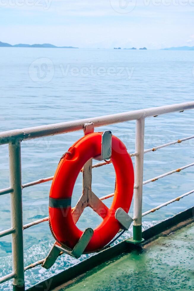 Bright Orange Lifebuoy on Ferry Deck with Ocean and Distant Islands in Background on a Clear Day photo