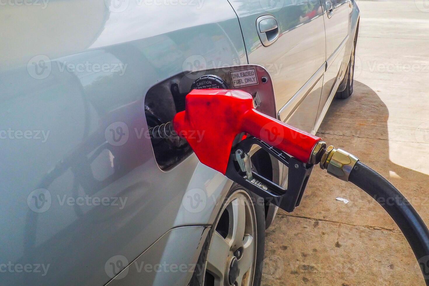 Close-Up of Red Fuel Pump Nozzle Refueling a Silver Car at a Gas Station on a Sunny Day photo