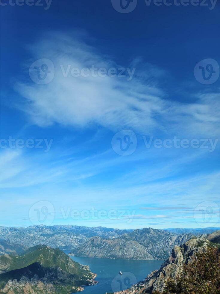 Panoramic Aerial View of the Bay of Kotor in Montenegro Surrounded by Majestic Mountains and Clear Blue Sky with White Clouds on a Sunny Day, Highlighting Natural Beauty and Tranquil Waters photo