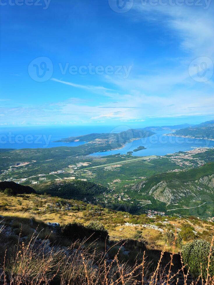 Vertical aerial view of the Bay of Kotor, Montenegro, with coastal towns, mountain ridges, and a bright blue sky with copy space. Ideal for travel promotions, posters, or social media backgrounds. photo