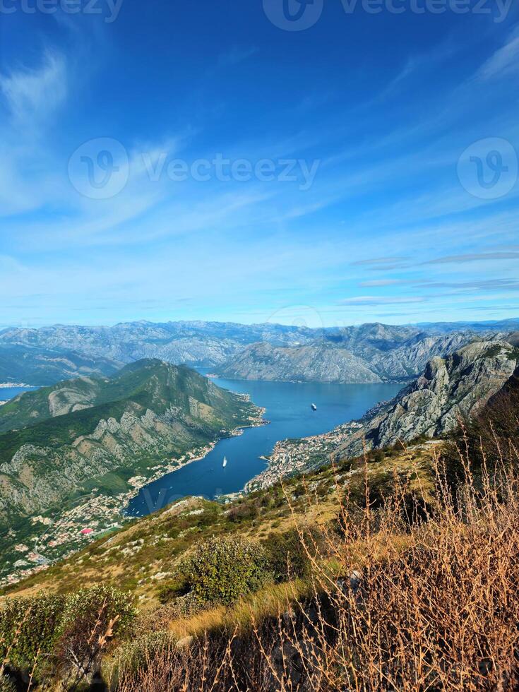 Vertical aerial view of the Bay of Kotor, Montenegro, with coastal towns, mountain ridges, and a bright blue sky with copy space. Ideal for travel promotions, posters, or social media backgrounds. photo