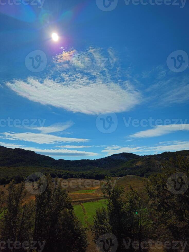 Vertical view of scenic valley with green meadows and surrounding hills under a bright sun and blue sky with clouds in Montenegro. Perfect for nature backgrounds, travel promotions, or eco-tourism ads photo