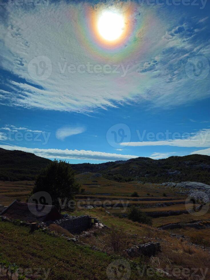 Vertical view of a sunlit rural landscape with terraced fields, stone structures, and rolling hills in Dolovi, Njegushi, under bright sky with a halo effect. Travel promotions or cultural tourism ads photo