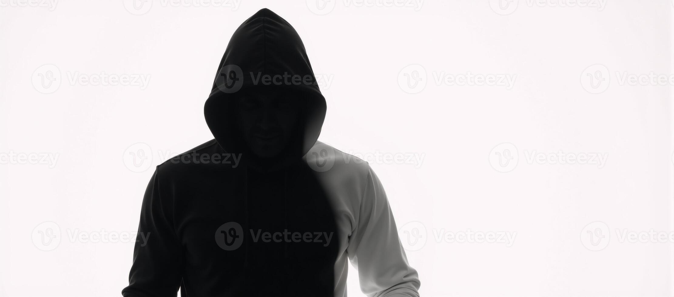 Dark isolated portrait of a hooded hacker in a black silhouette against a stark white backdrop photo