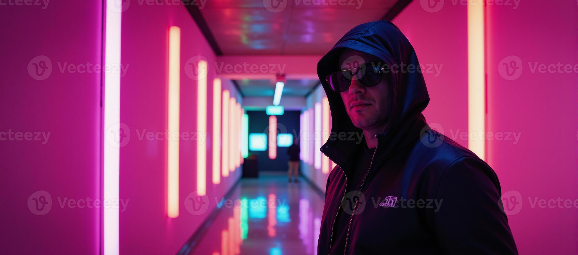 A hooded man stands in a vibrant neonlit futuristic hall photo